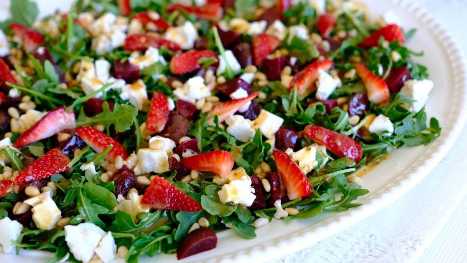 A plate of arugula salad topped with strawberries, feta cheese, nuts, and a light drizzle of dressing.