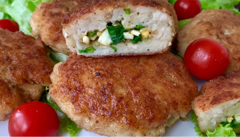 Golden-brown breaded cutlets filled with chopped eggs and herbs, served on lettuce leaves with cherry tomatoes.
